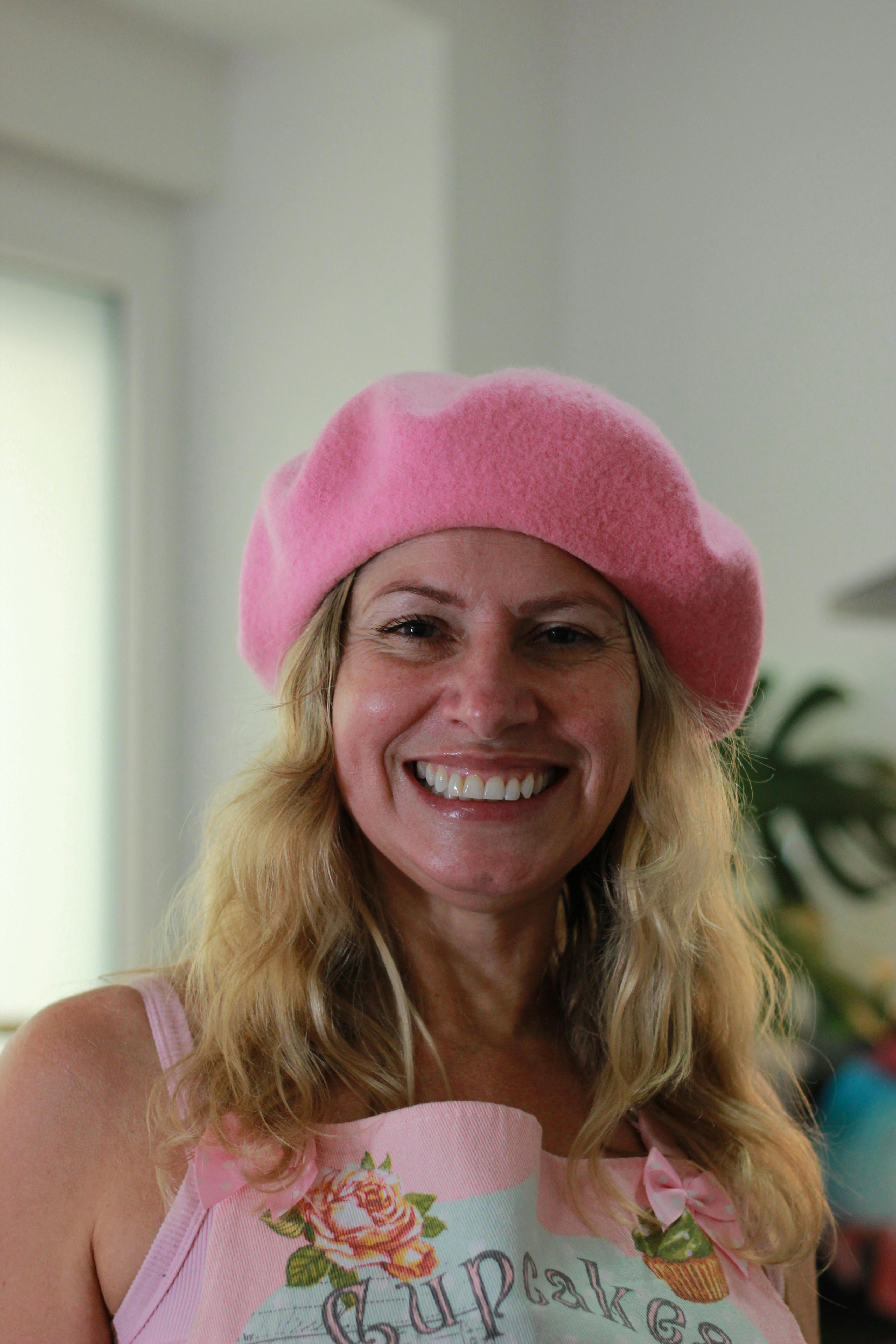 Woman with a beaming smile wearing a pink beret and apron in a cozy kitchen.
