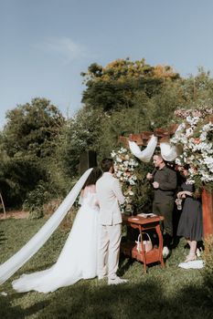 Elegant outdoor wedding ceremony under a flower-draped arch on a sunny day.