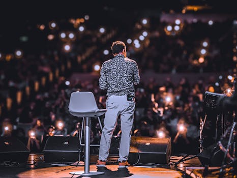 Speaker addressing large audience with phones lit up at night event.