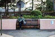 一名男子坐在公园的长凳上，周围绿植环绕，正全神贯注地玩着智能手机