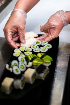A chef carefully arranges a variety of sushi rolls on a black tray, showcasing culinary art.