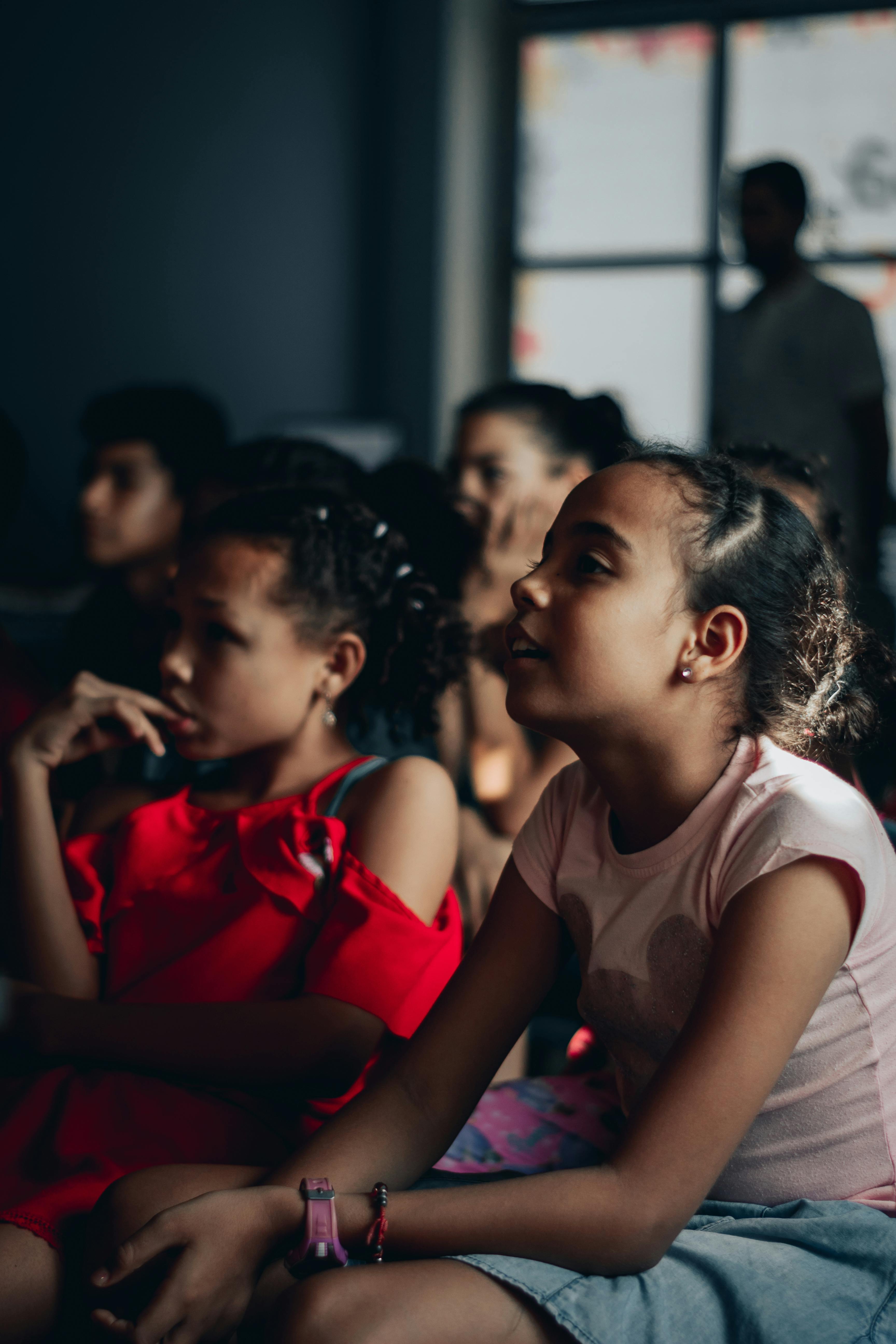 Free A group of children attentively watching a performance in a dimly lit room. Stock Photo