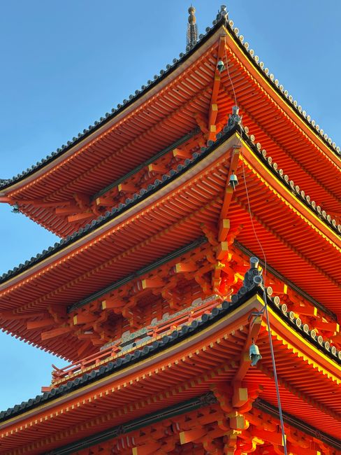 A close-up of a vibrant red pagoda with intricate details against a clear blue sky in Kyoto, Japan.