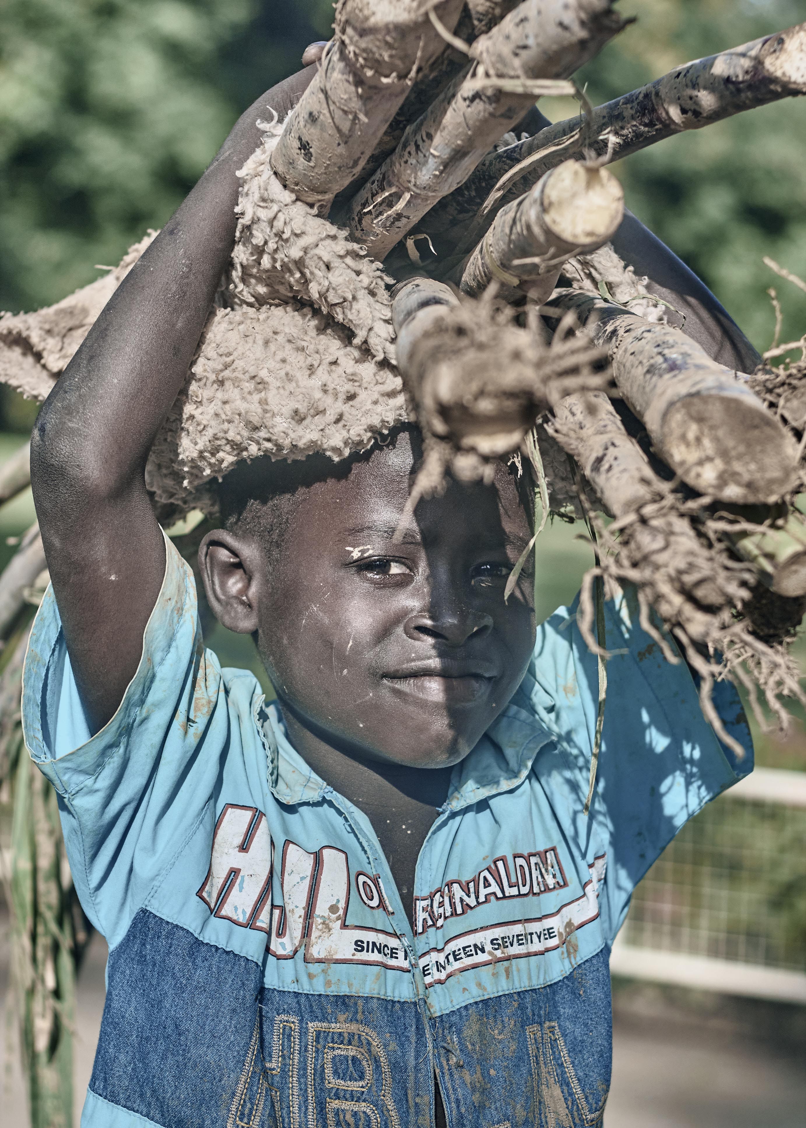 A young boy carries firewood on his head, showcasing daily life in a rural environment.