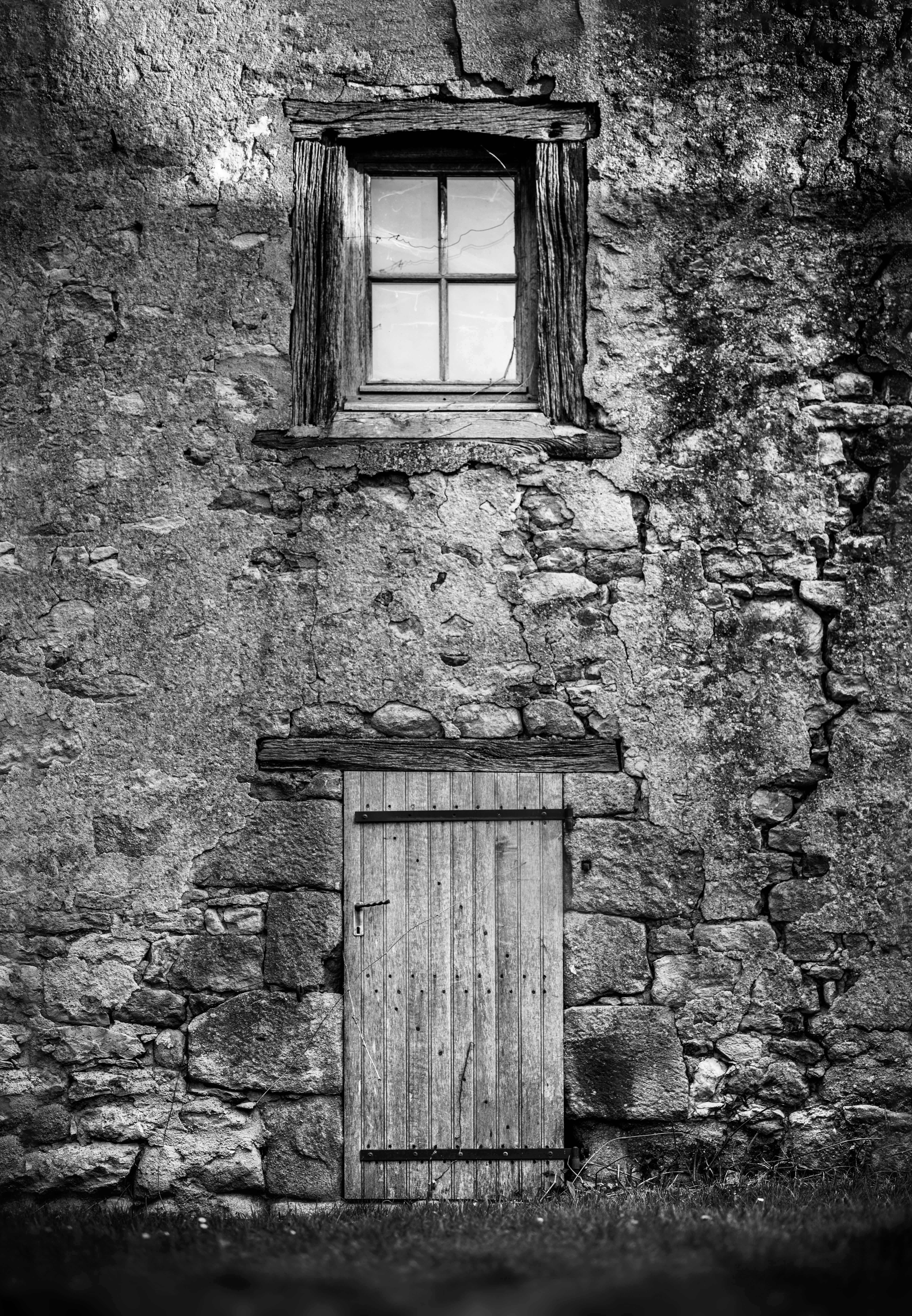 Black and white image of a rustic stone wall with a wooden door and window, vintage style.