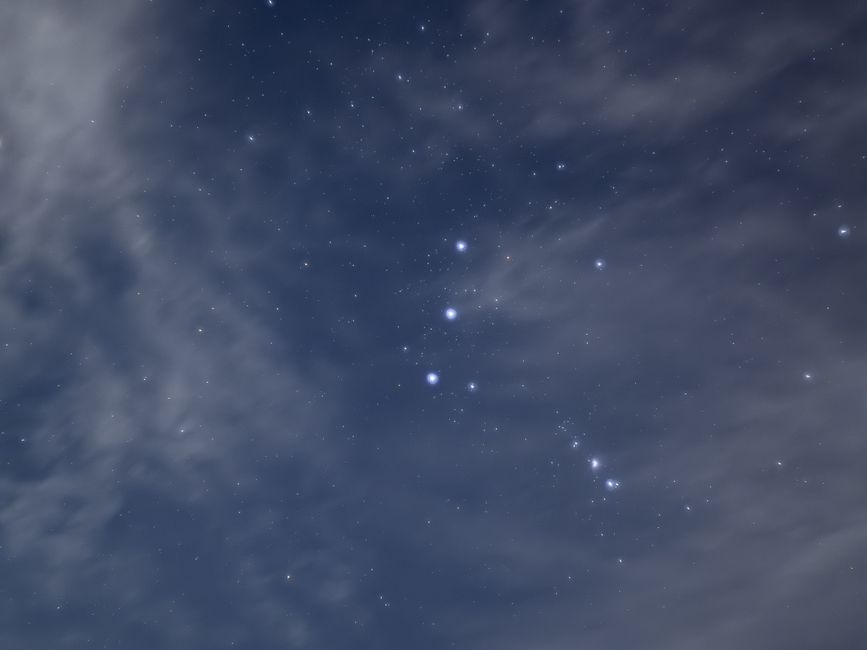 Vista deslumbrante da constelação de Órion cercada por nuvens e estrelas no céu noturno.