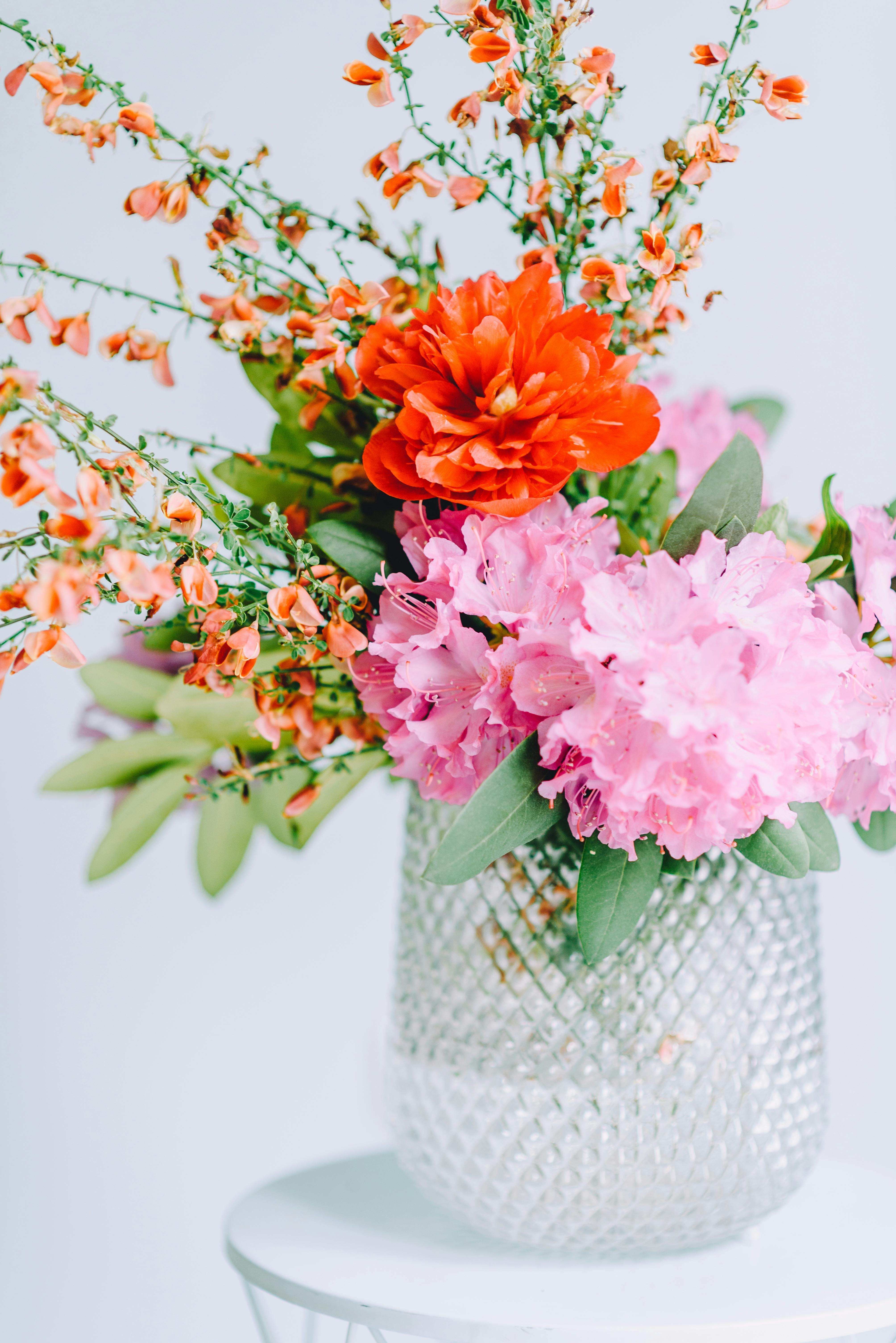 Bright arrangement of pink rhododendrons and orange flowers in a crystal vase, perfect for spring decor.