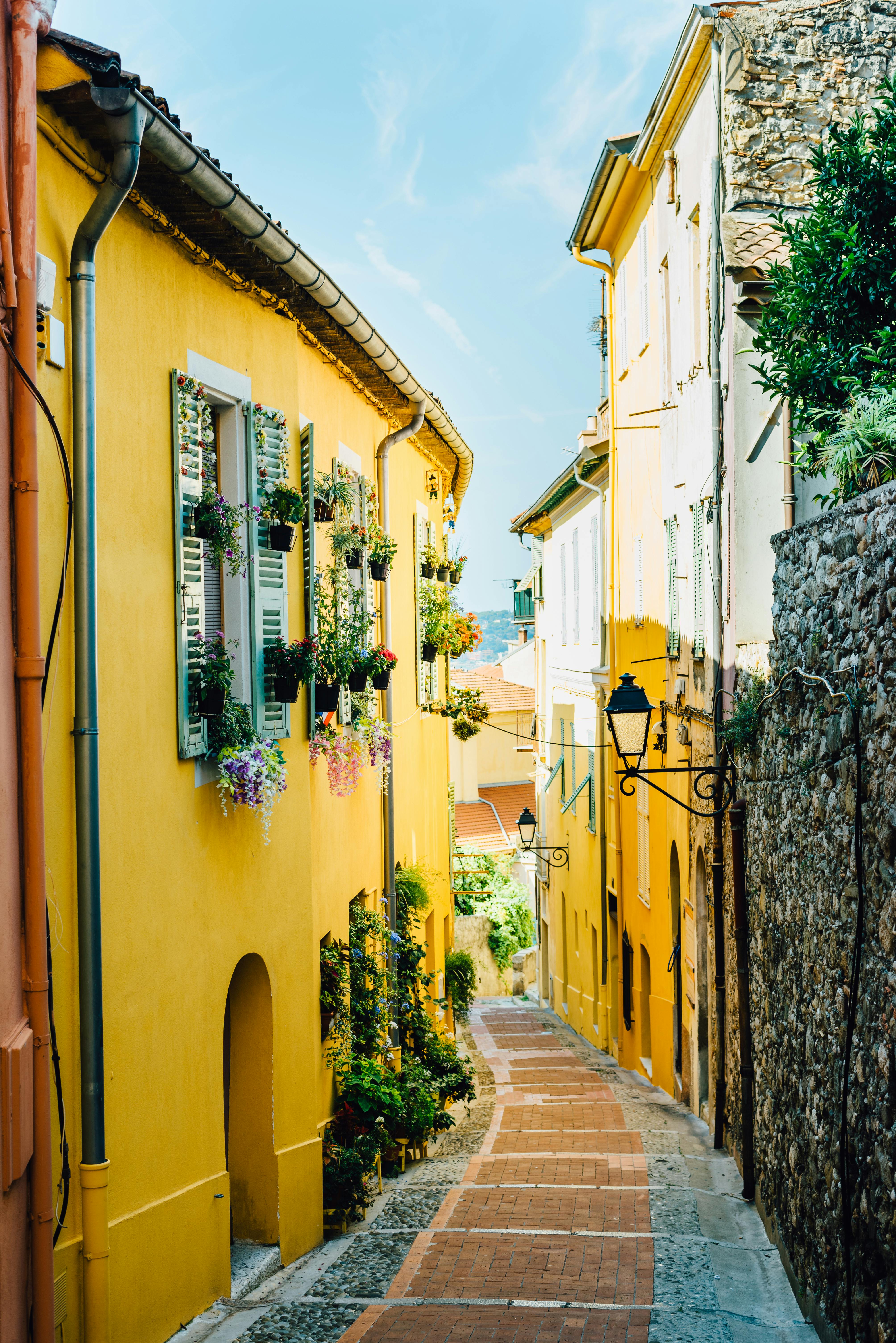 A picturesque narrow street with vibrant yellow buildings and floral decorations in a Mediterranean setting.