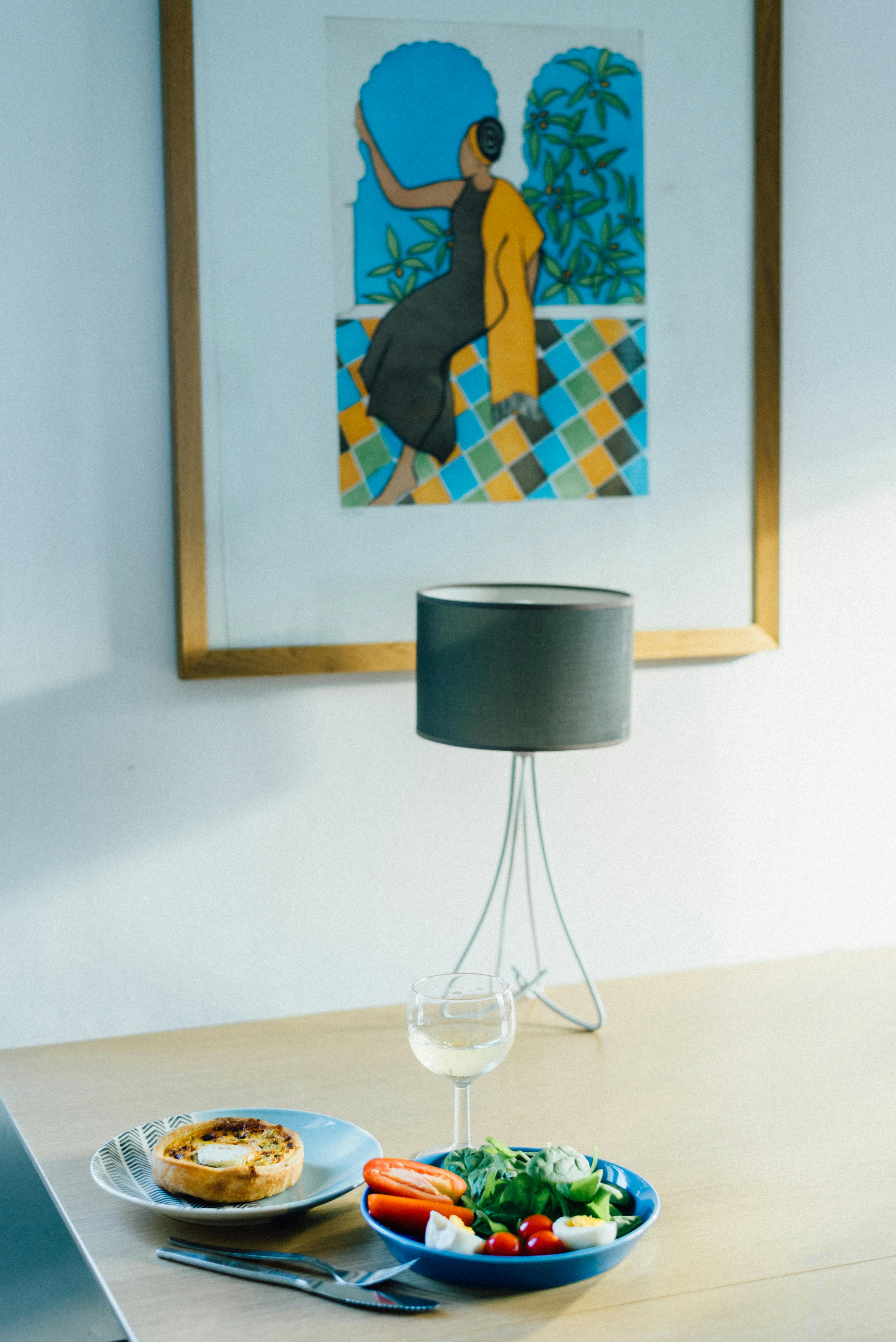 A serene dining setup with a salad and tart, and art piece in a modern interior.