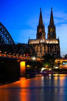 Dramatic night view of Cologne Cathedral with its reflection in the Rhine, showcasing architectural beauty.