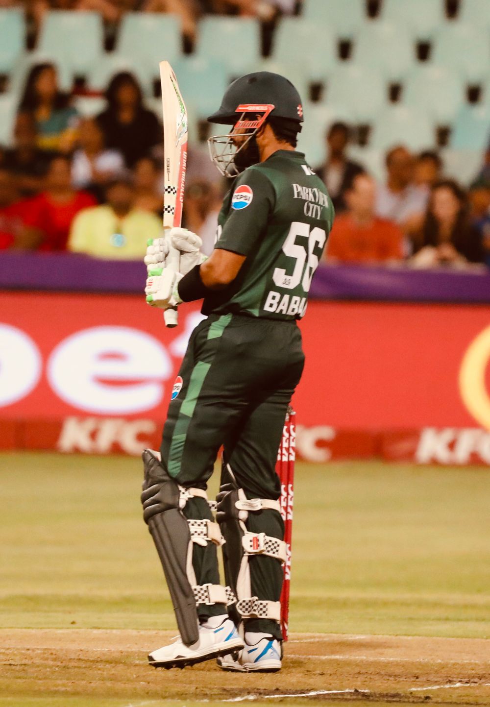 Cricket player in green match uniform holding a bat