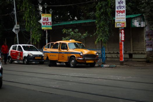 Iconic yellow taxi parked on a bustling street in Kolkata, India, capturing urban life.