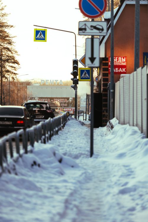 Free A snowy sidewalk in an urban area with traffic signs and parked cars during daylight. Stock Photo