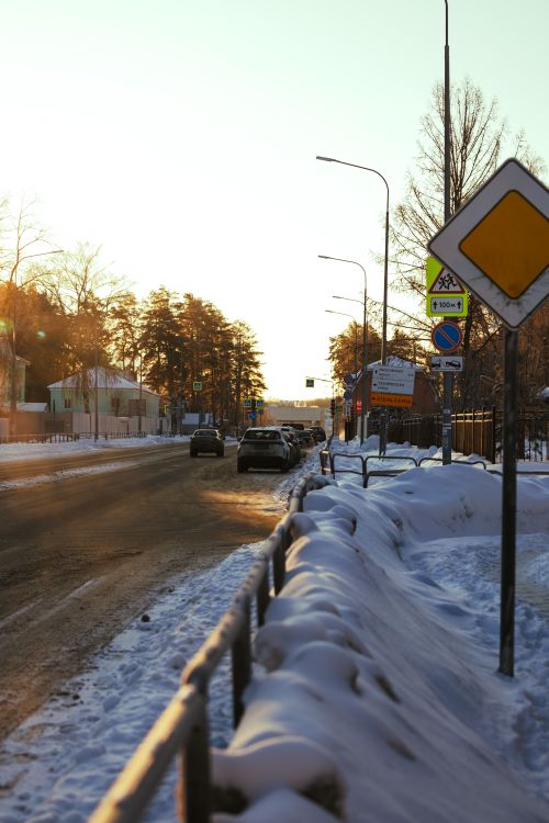 Free A snowy urban street at sunset with cars and road signs on a clear winter day. Stock Photo