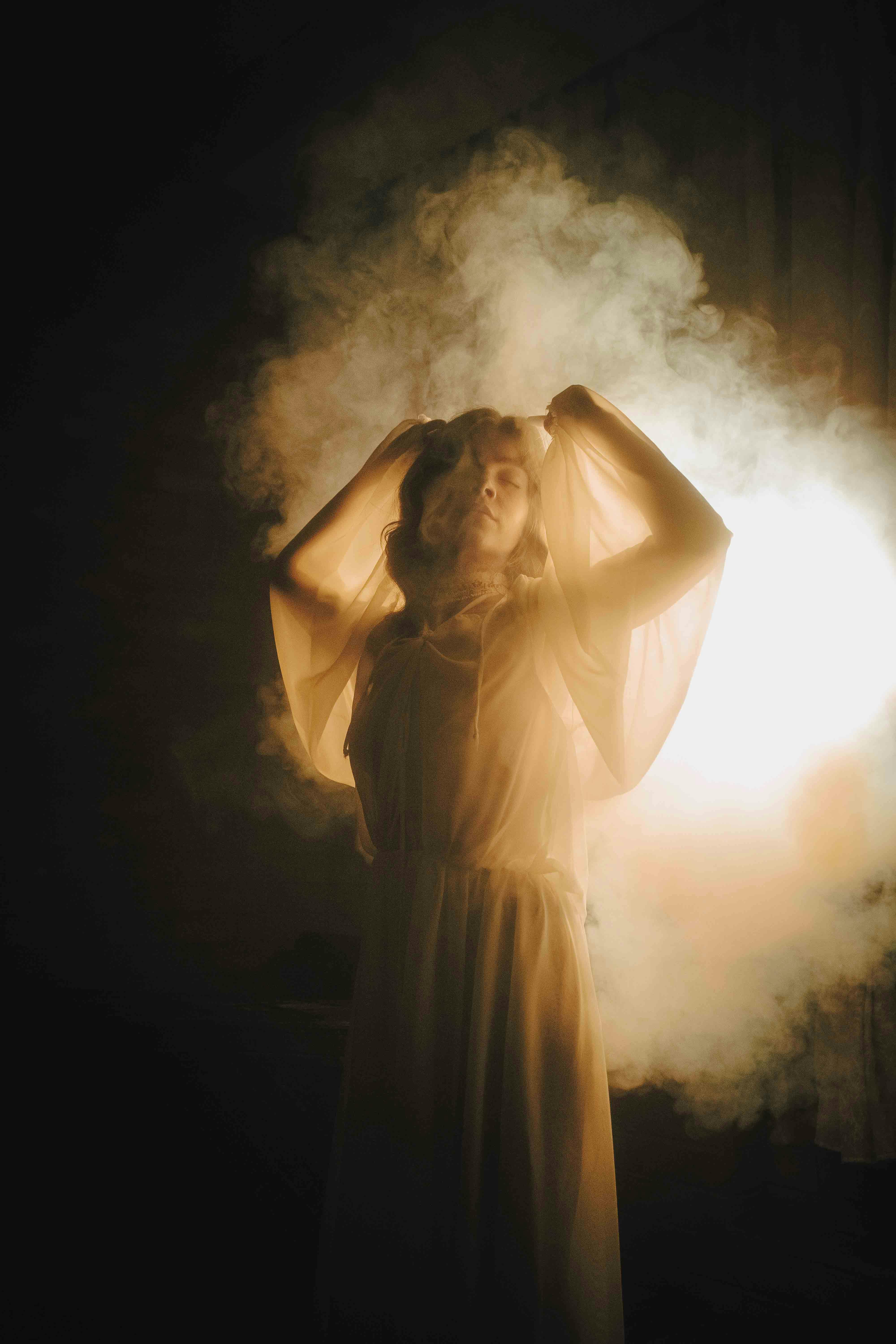 A woman enveloped in mist, illuminated by soft, warm lighting, creating an ethereal atmosphere.