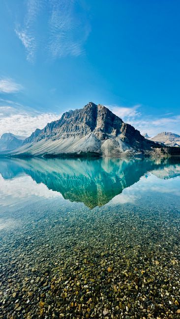Majestic mountain reflected in clear blue lake under a bright sky, offering a serene nature view.