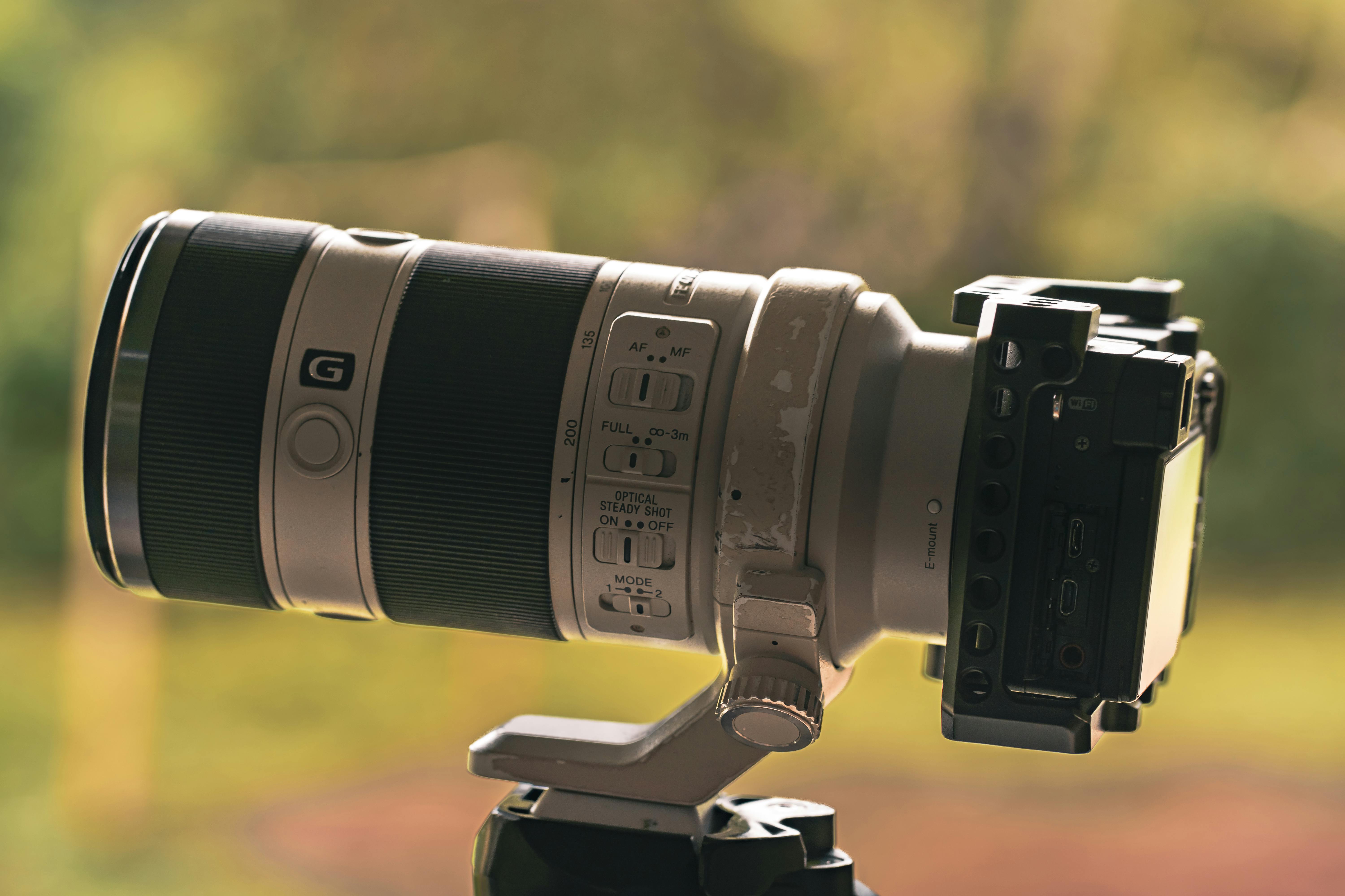 Detailed view of a high-end camera lens mounted outdoors against a blurred natural background.