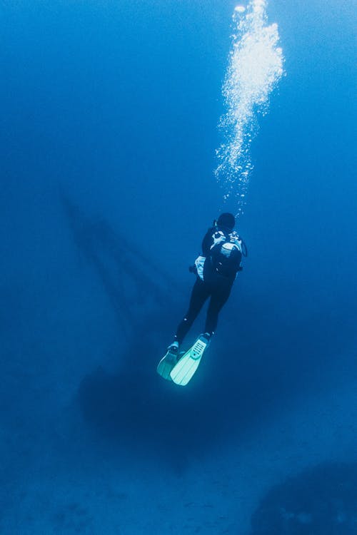 Faceless diver in equipment exploring blue ocean water