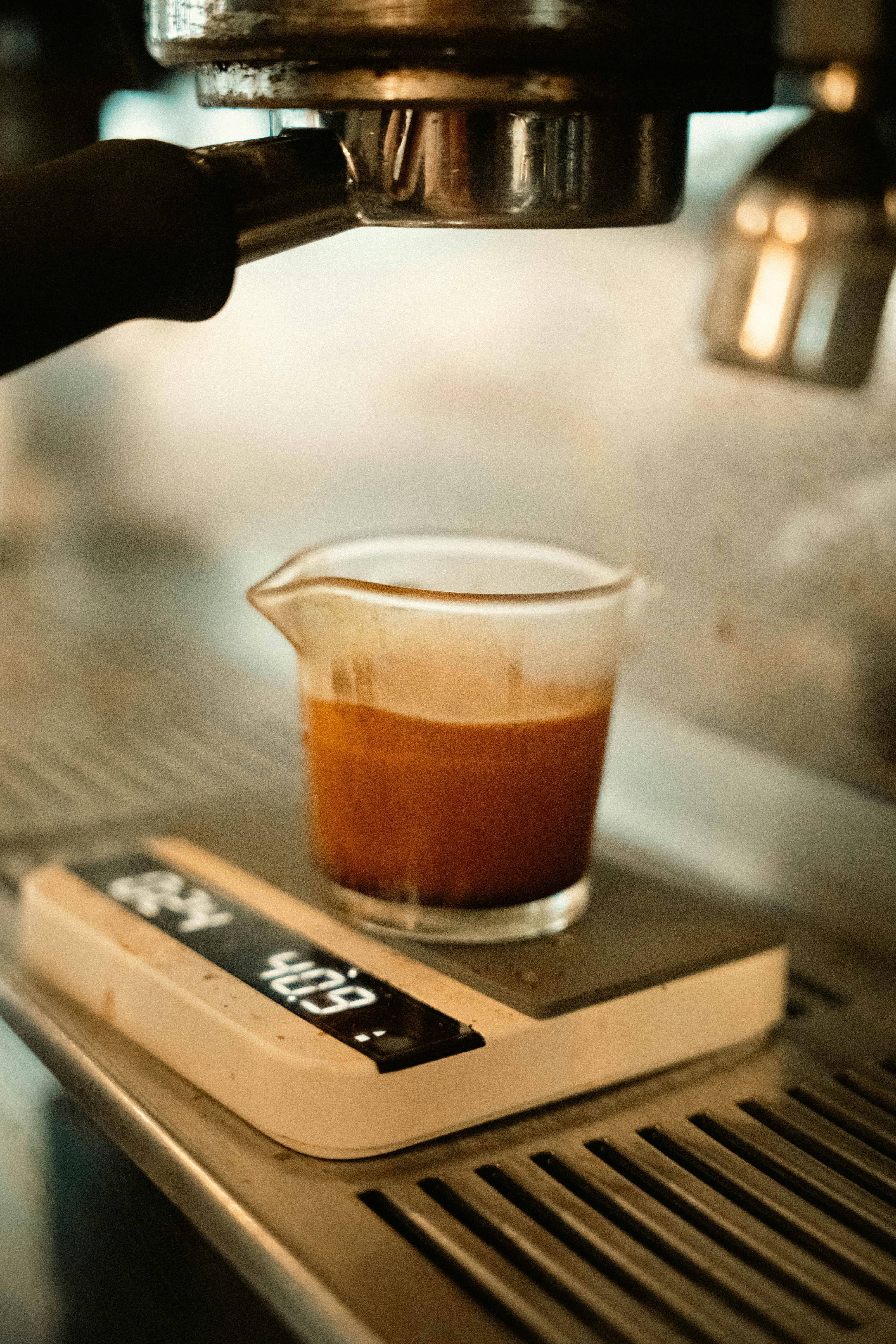 Hand pouring coffee into a cup beside a scale for repeatable brews