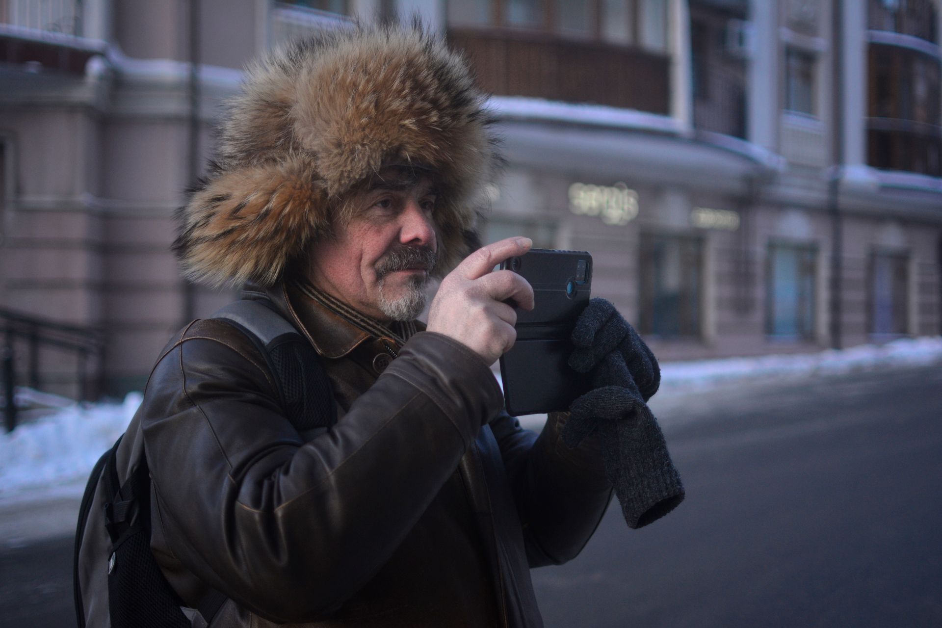 Adult man wearing a fur hat photographing outdoors in winter.