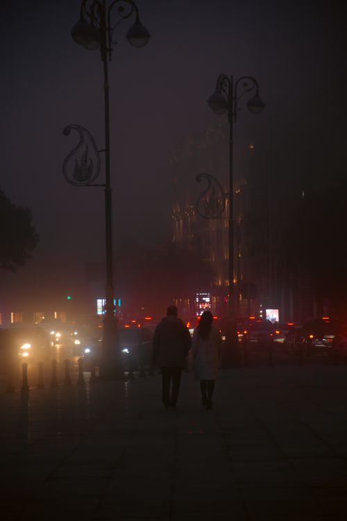 Free A foggy city street at night with silhouettes of people and glowing traffic lights. Stock Photo