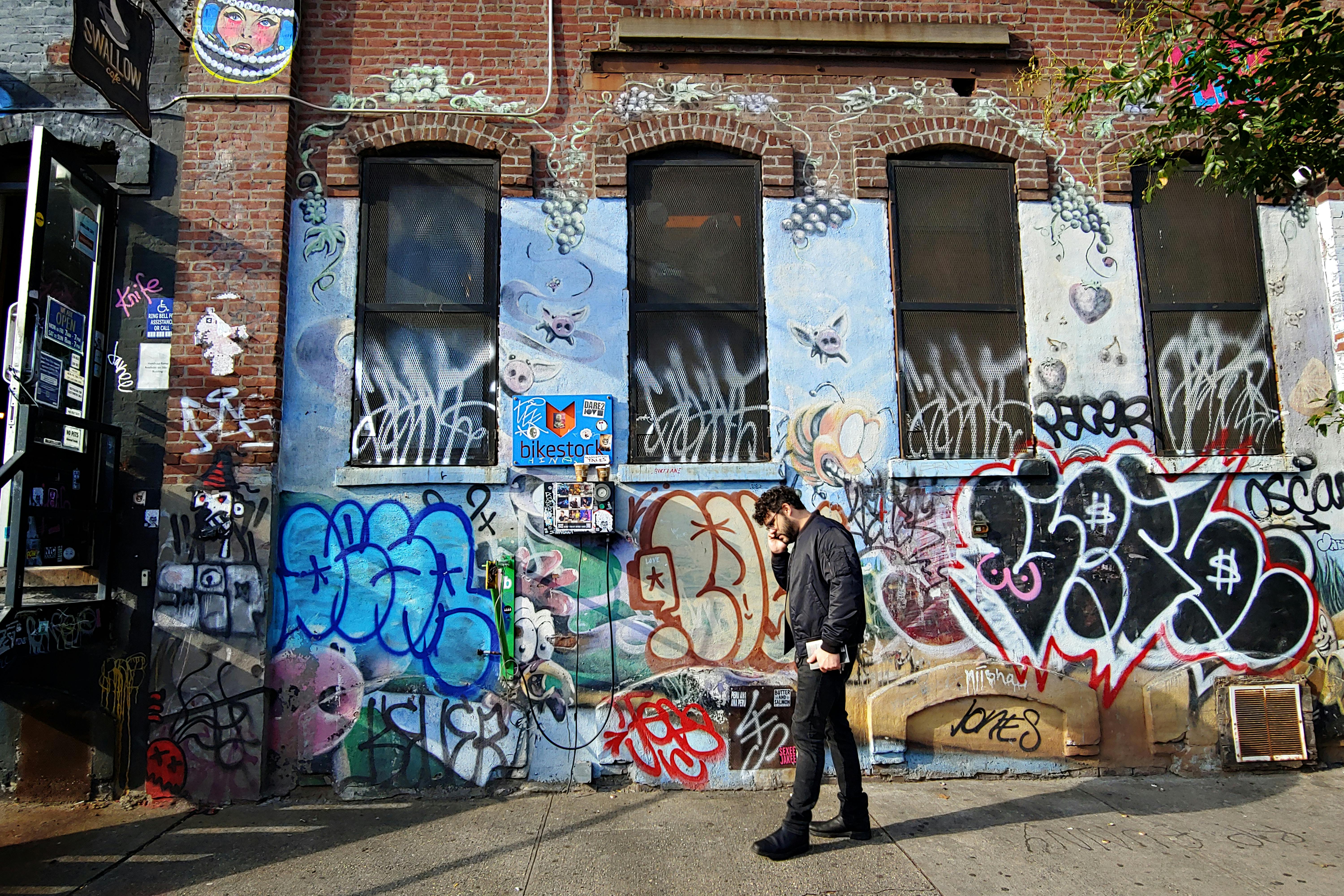 Vibrant graffiti alley in Brooklyn with a person walking by, capturing urban street art culture.
