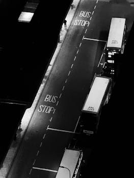 Black and white aerial shot of a city bus stop at night with several buses.