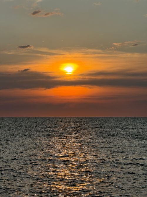 Free Dramatic sunset over the ocean with vibrant orange and yellow hues reflecting on the water. Stock Photo