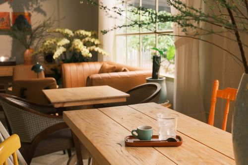 Free Warm, inviting café interior with wooden tables, plants, and soft seating. Stock Photo