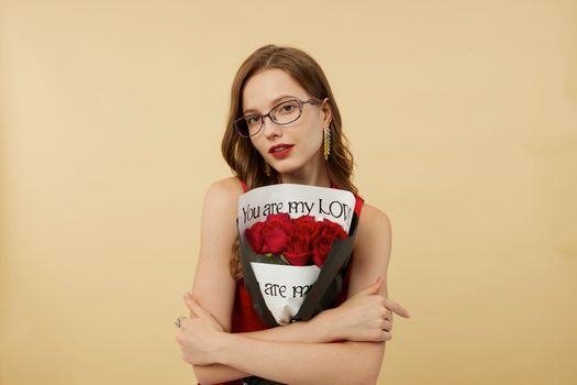 Elegantly dressed woman with glasses holding a bouquet of red roses against a soft beige background.