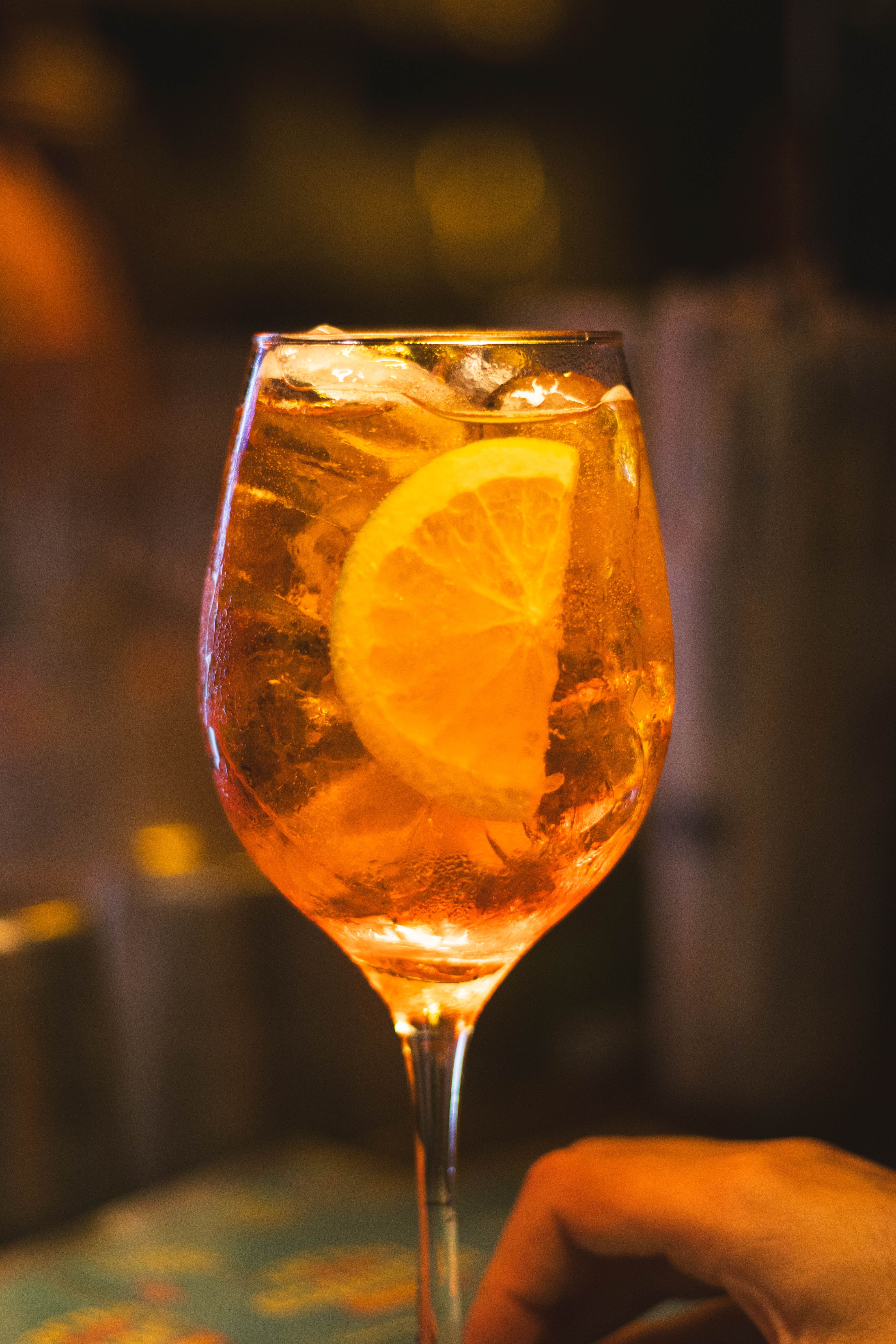 A glass of Aperol spritz with prosecco and soda water, garnished with a half orange slice and ice cubes, next to the orange-red Aperol bottle.