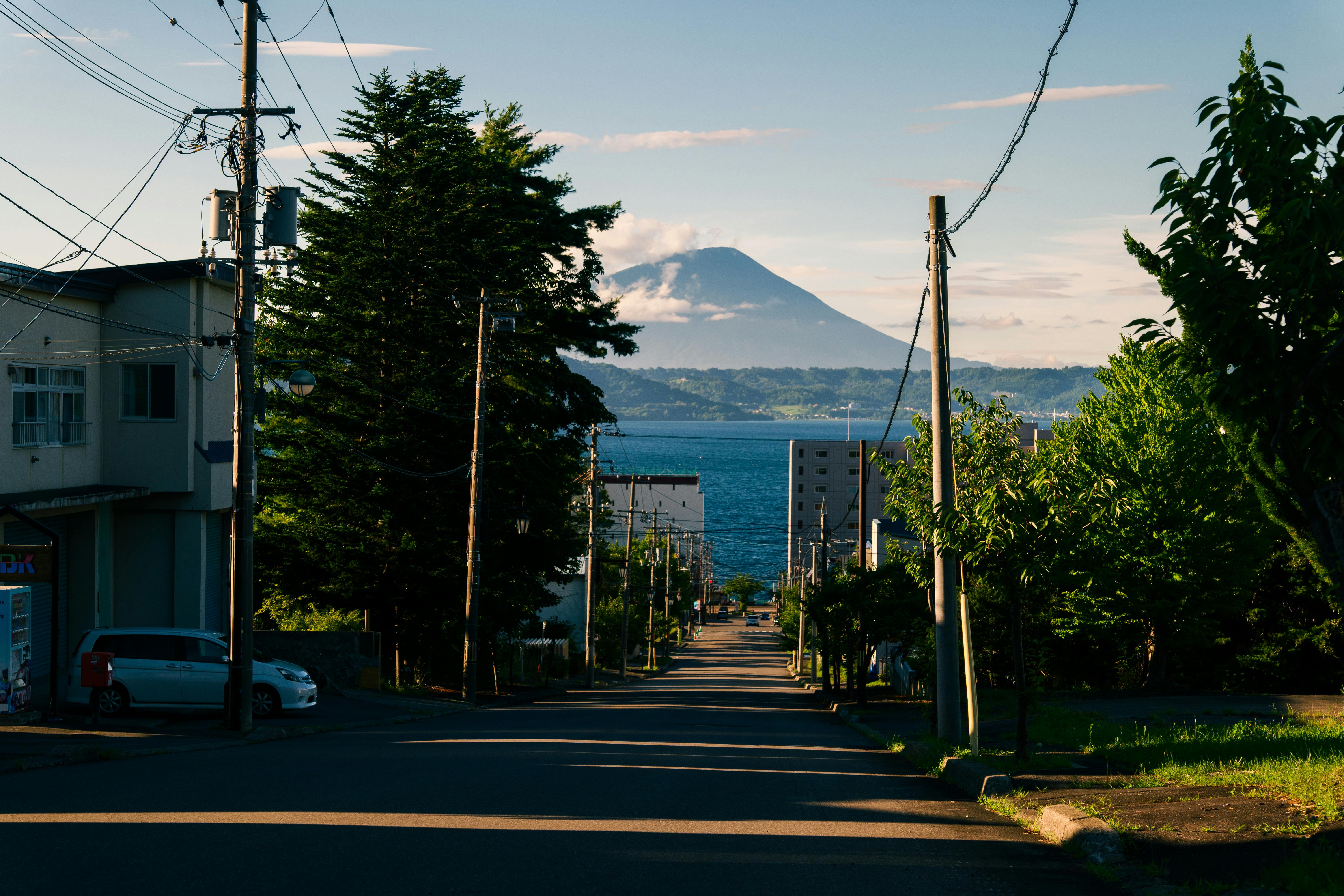 Street leading to scenic mountain view with lush greenery and ocean in sight.