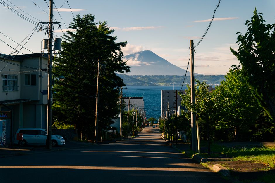 Street leading to scenic mountain view with lush greenery and ocean in sight.