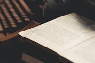 一本打开的书放在一台古董打字机前，书页上可见文字，唤起了复古文学主题