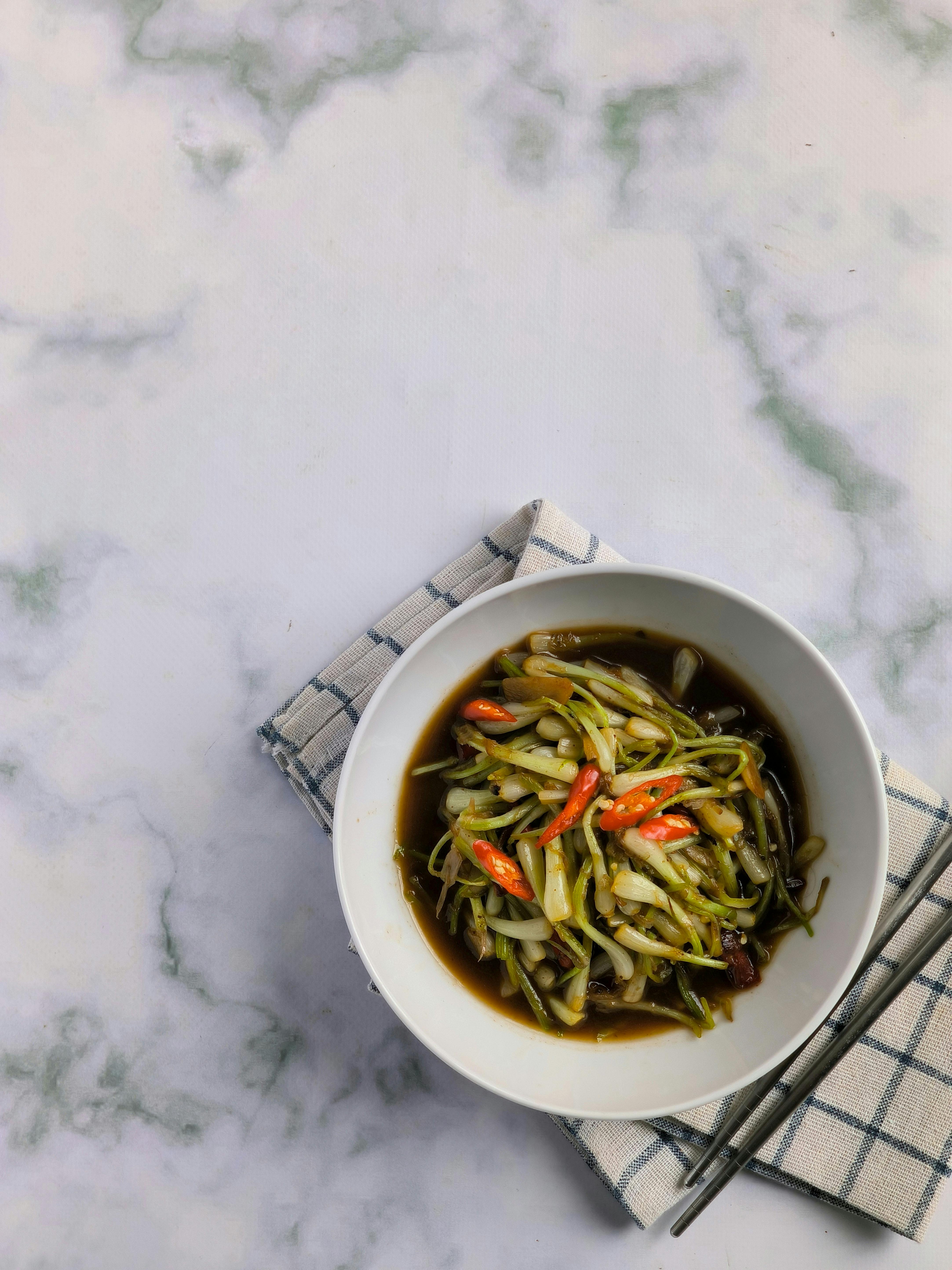 Top view of Asian vegetable stir fry with beans and chili in a white bowl, served on a plaid napkin.
