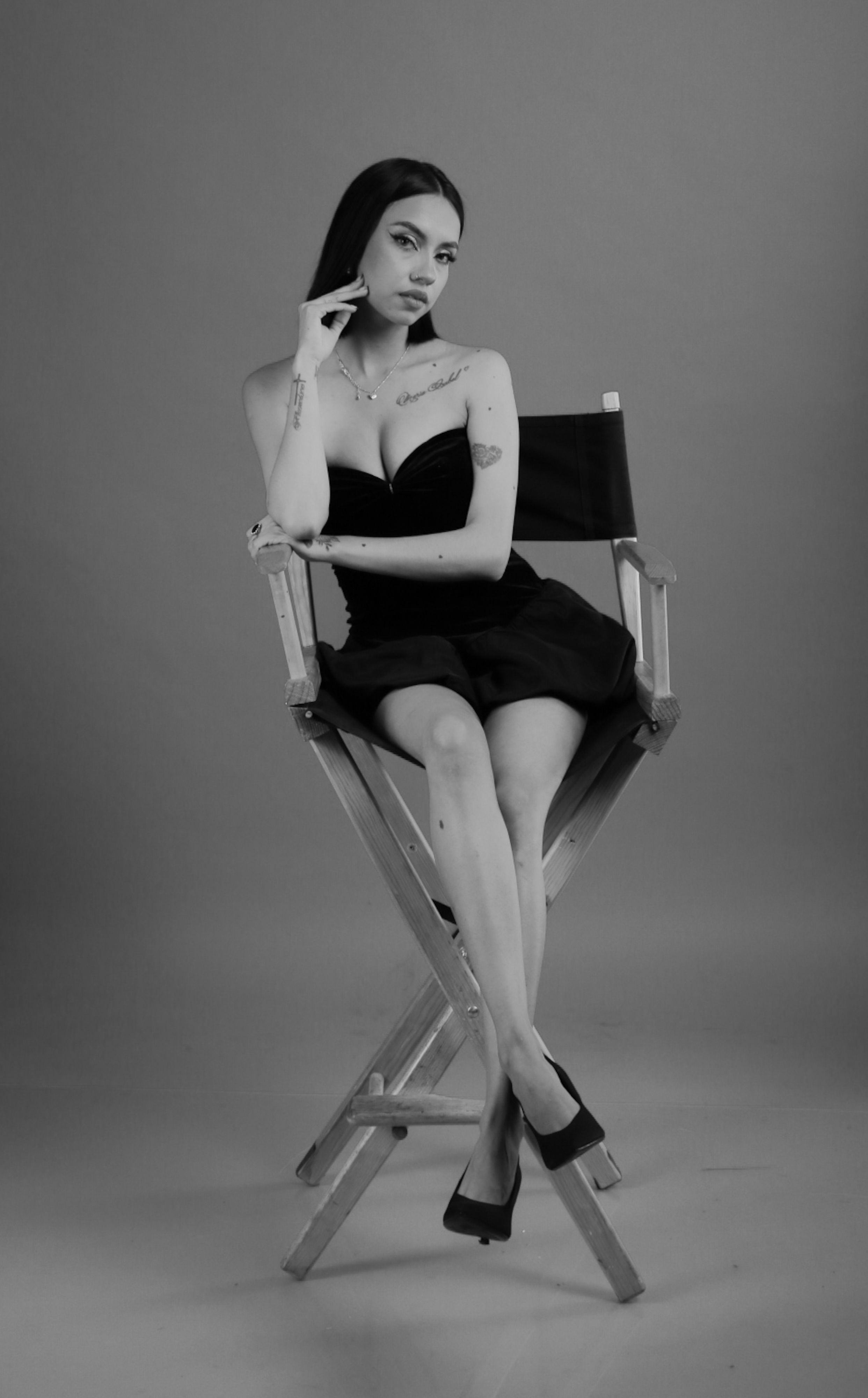 Elegant black and white portrait of a woman sitting on a director's chair, exuding confidence and style.