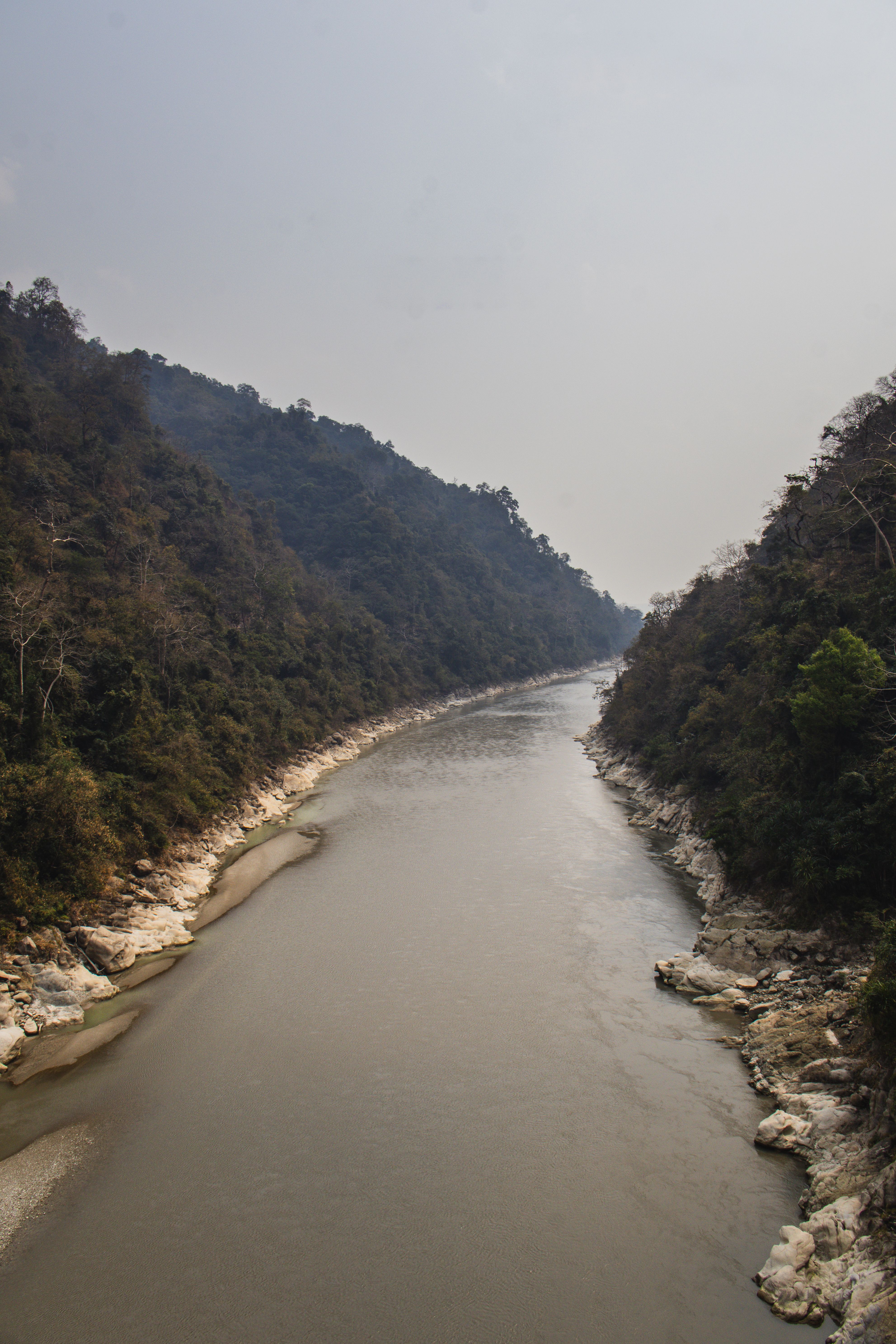 A picturesque river flows between forested hillsides under a cloudy sky.