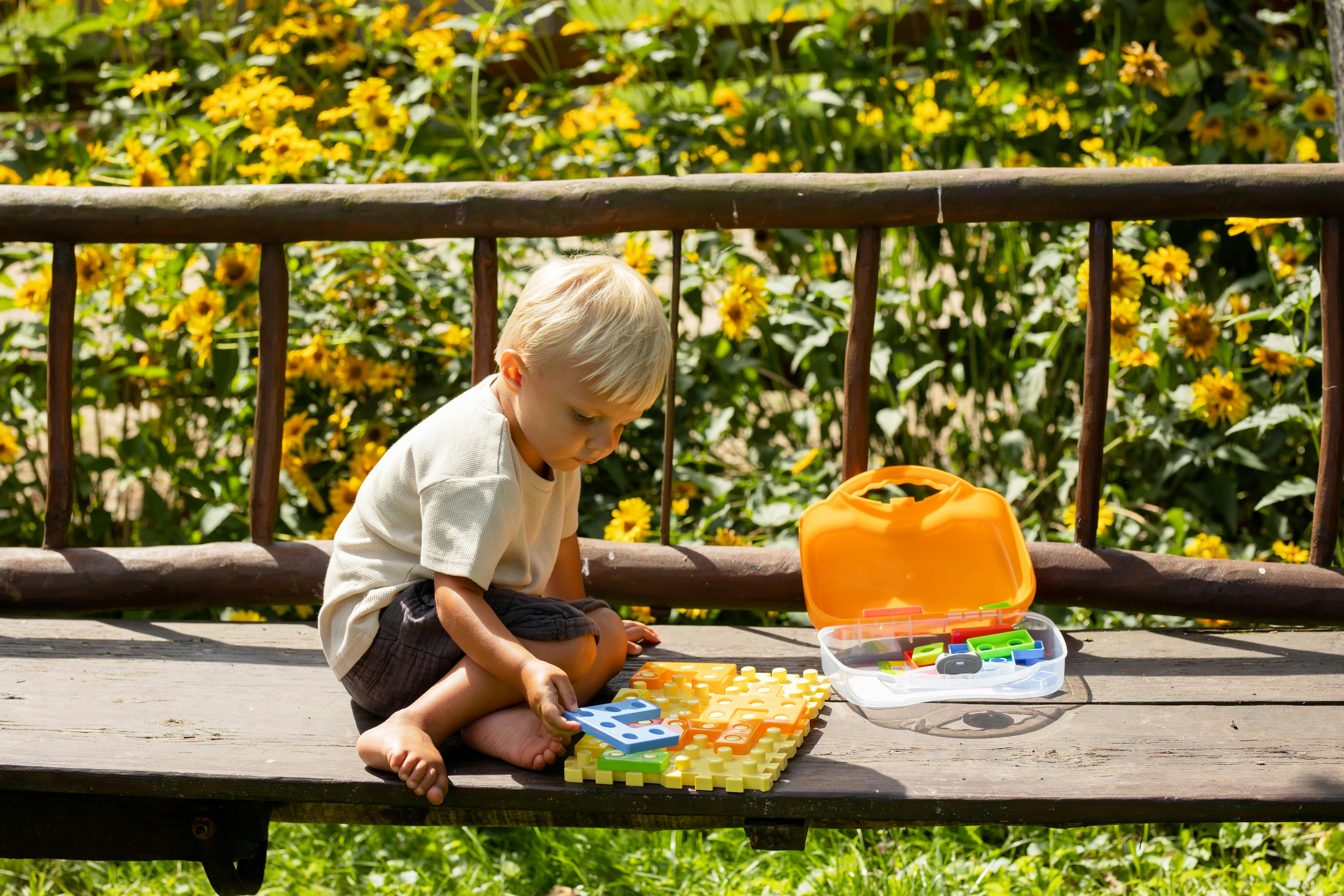 A young boy playing with a colorful puzzle outdoors on a sunny summer day.