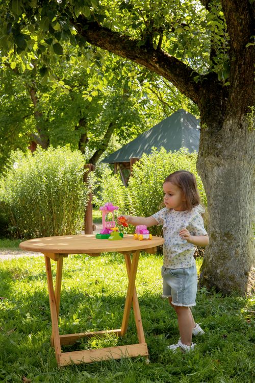 Free A young girl plays with colorful toys on a table in a lush summer garden under a tree. Stock Photo
