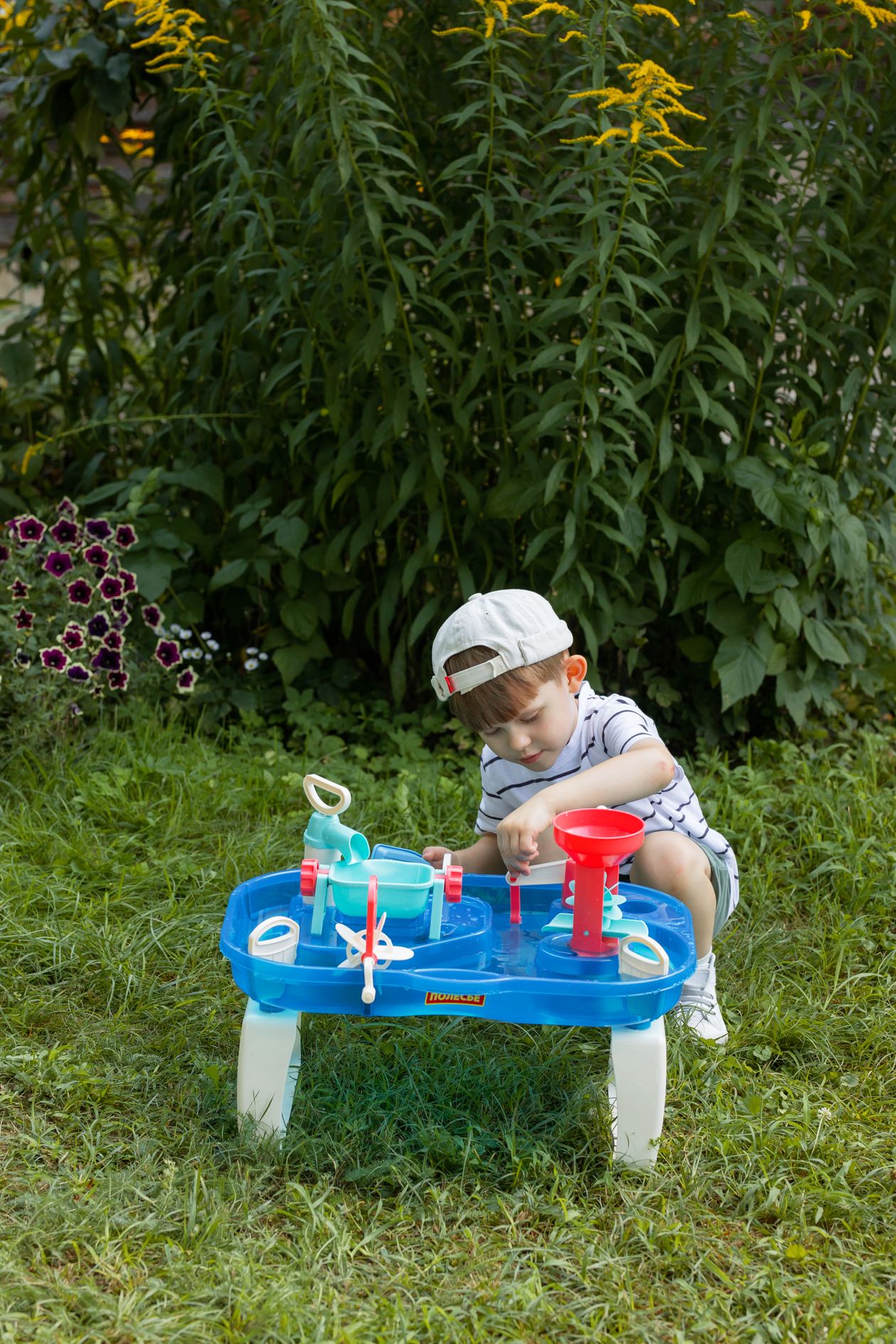 Young child playing outdoors with a water toy table, an outdoor activity for 1 year olds