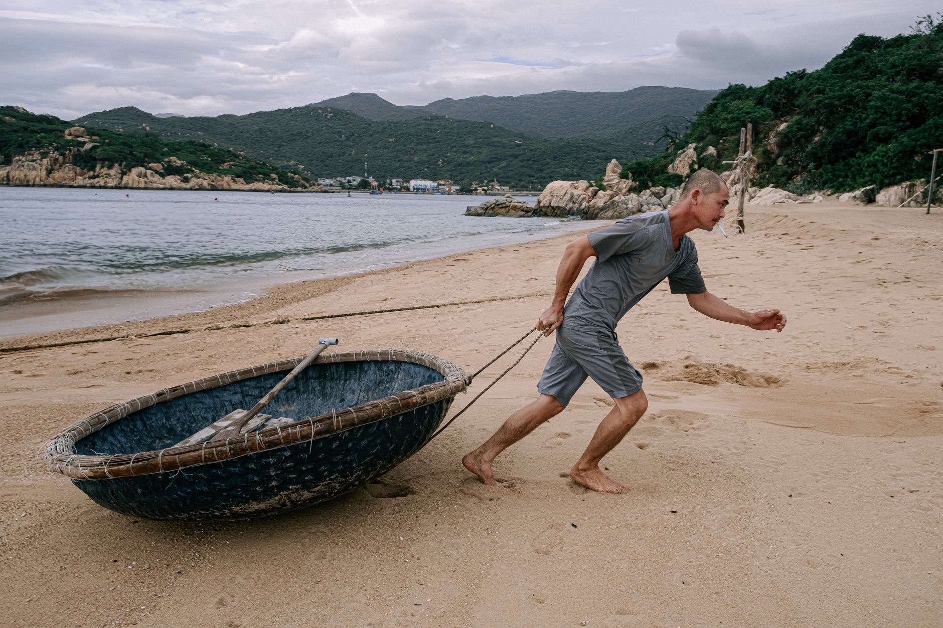 Man pulling a traditional Vietnamese basket boat on a Ninh Thuận beach, showcasing local culture and coastal landscape.
