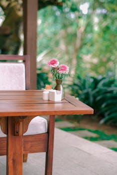 A vase of pink flowers on a wooden table against a lush garden backdrop.