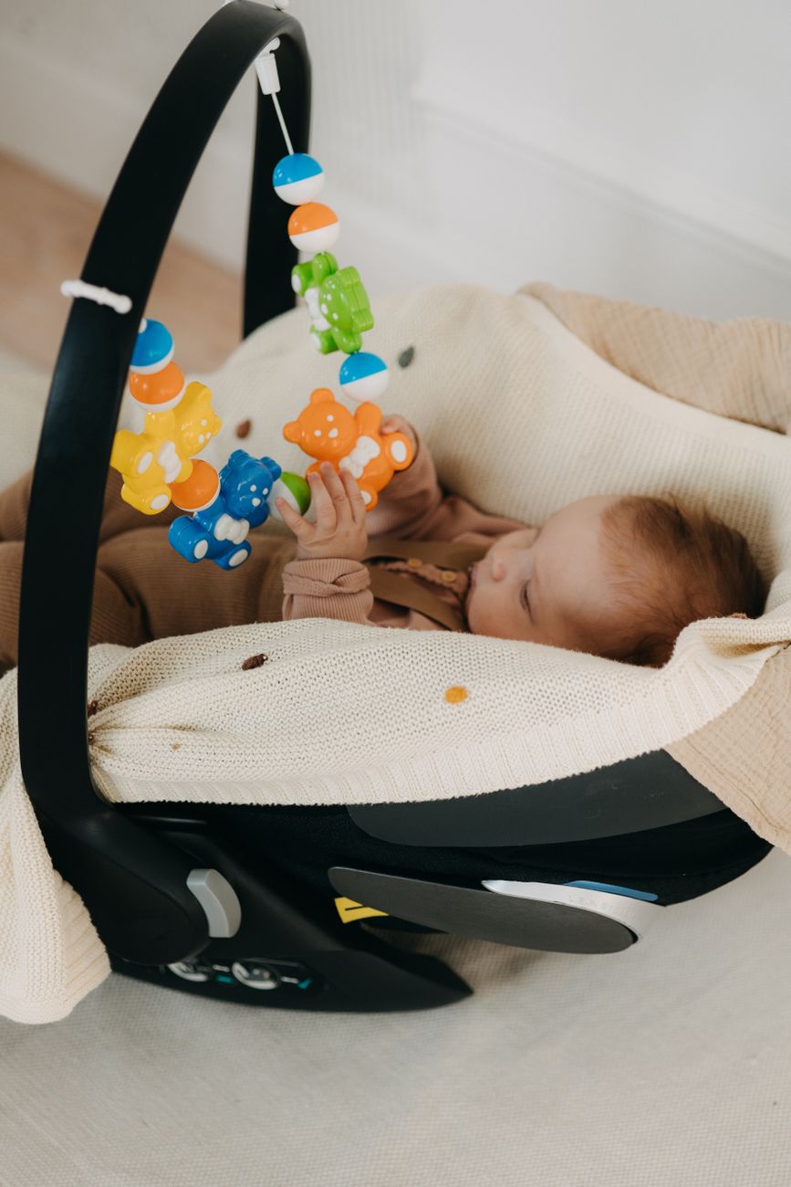 Bebê em cadeirinha de carro brincando com brinquedos coloridos pendurados