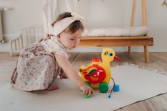 Cute baby girl playing with a colorful duck toy on a white rug in a cozy room.