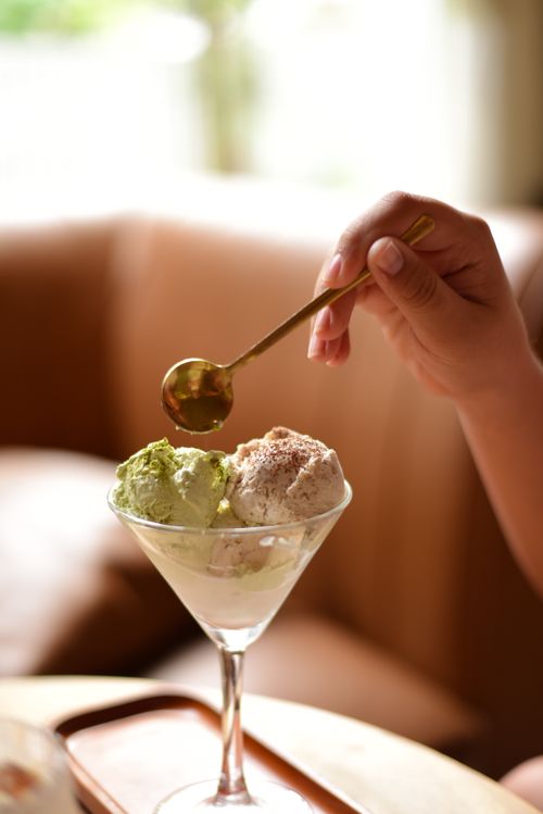 Free Hand holding spoon over ice cream in elegant glass bowl, indoor setting. Stock Photo