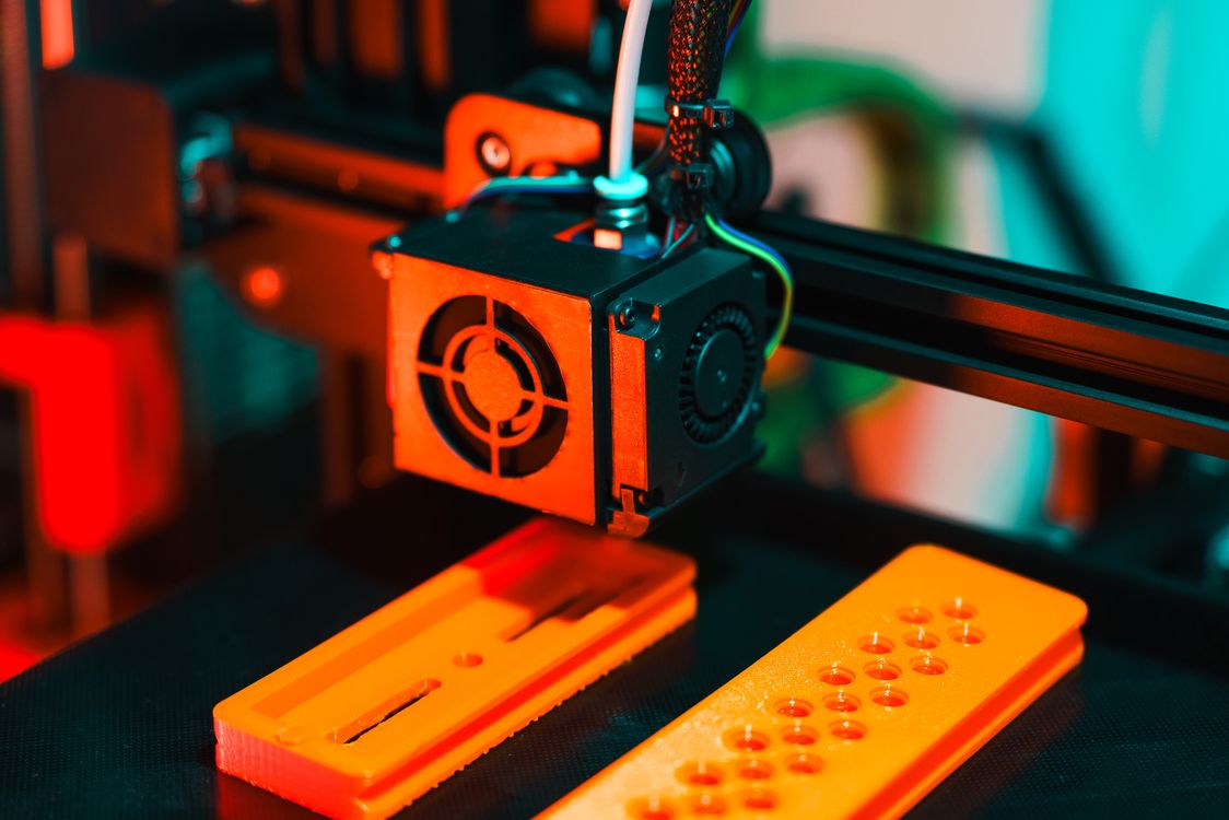 Close-up of a 3D printer extruding orange plastic filament