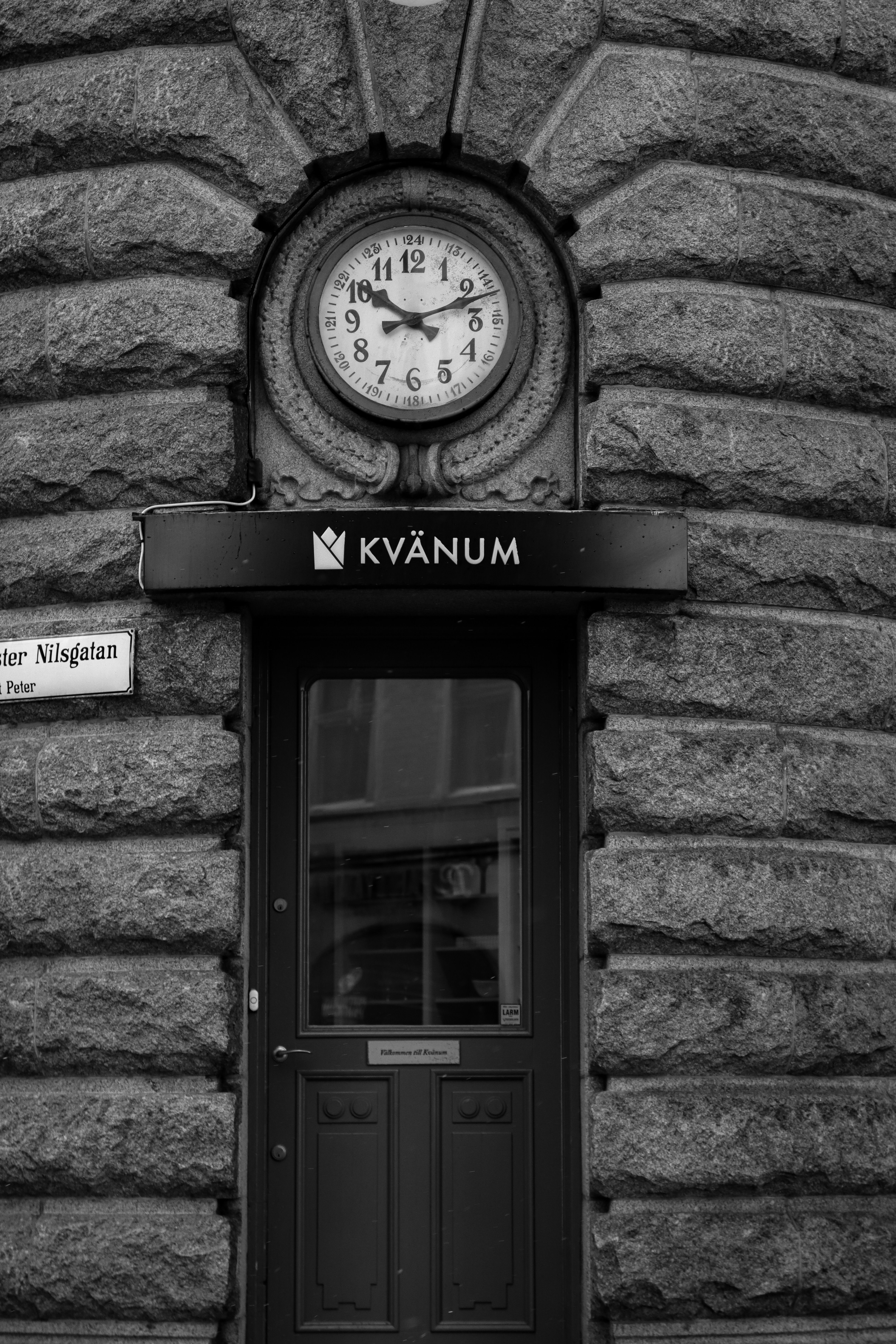 Black and white photo of a vintage clock above a door in Malmö, Sweden.