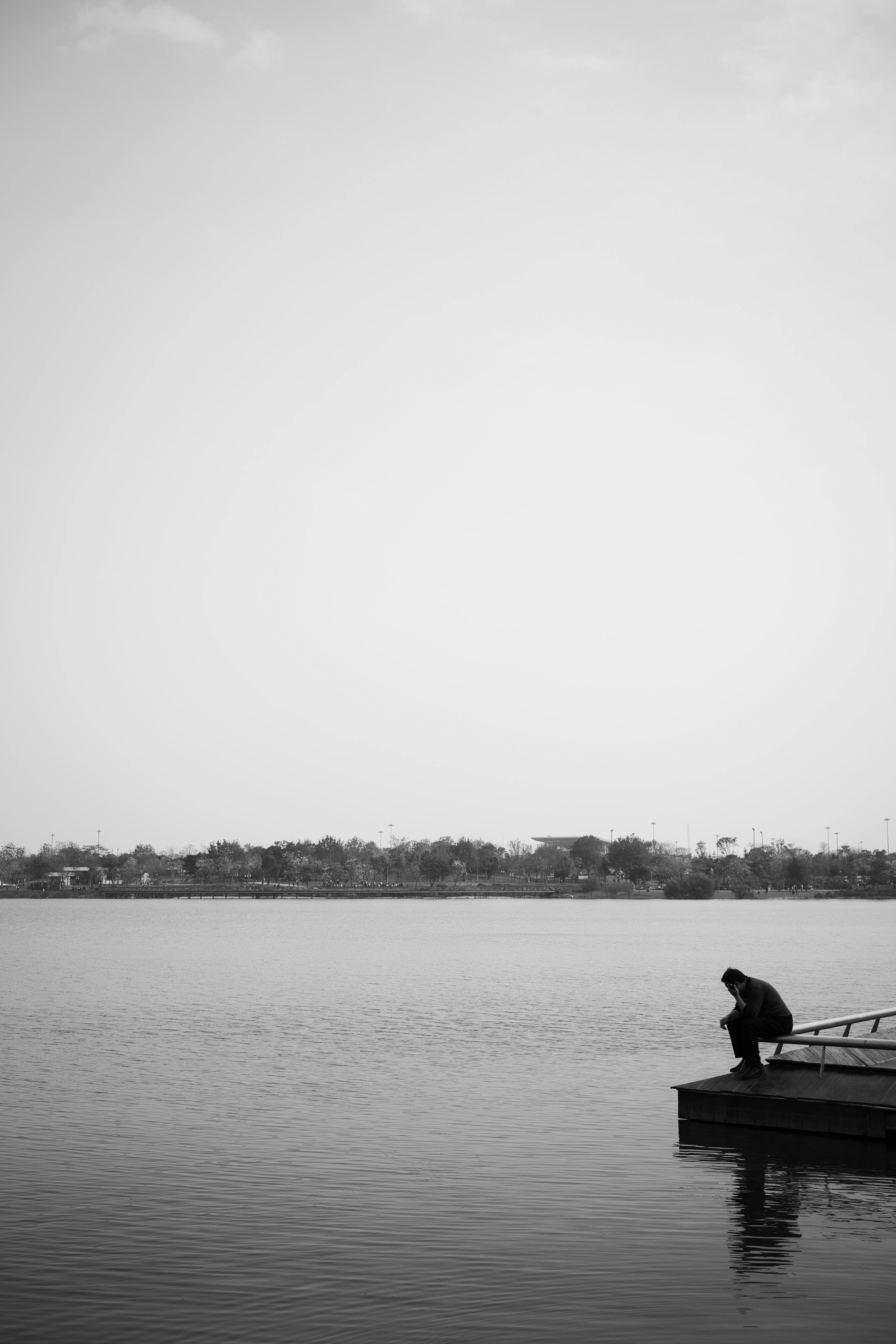 A solitary person sits on a pier, gazing over calm waters, evoking tranquility.