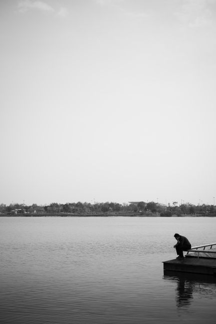 A solitary person sits on a pier, gazing over calm waters, evoking tranquility.