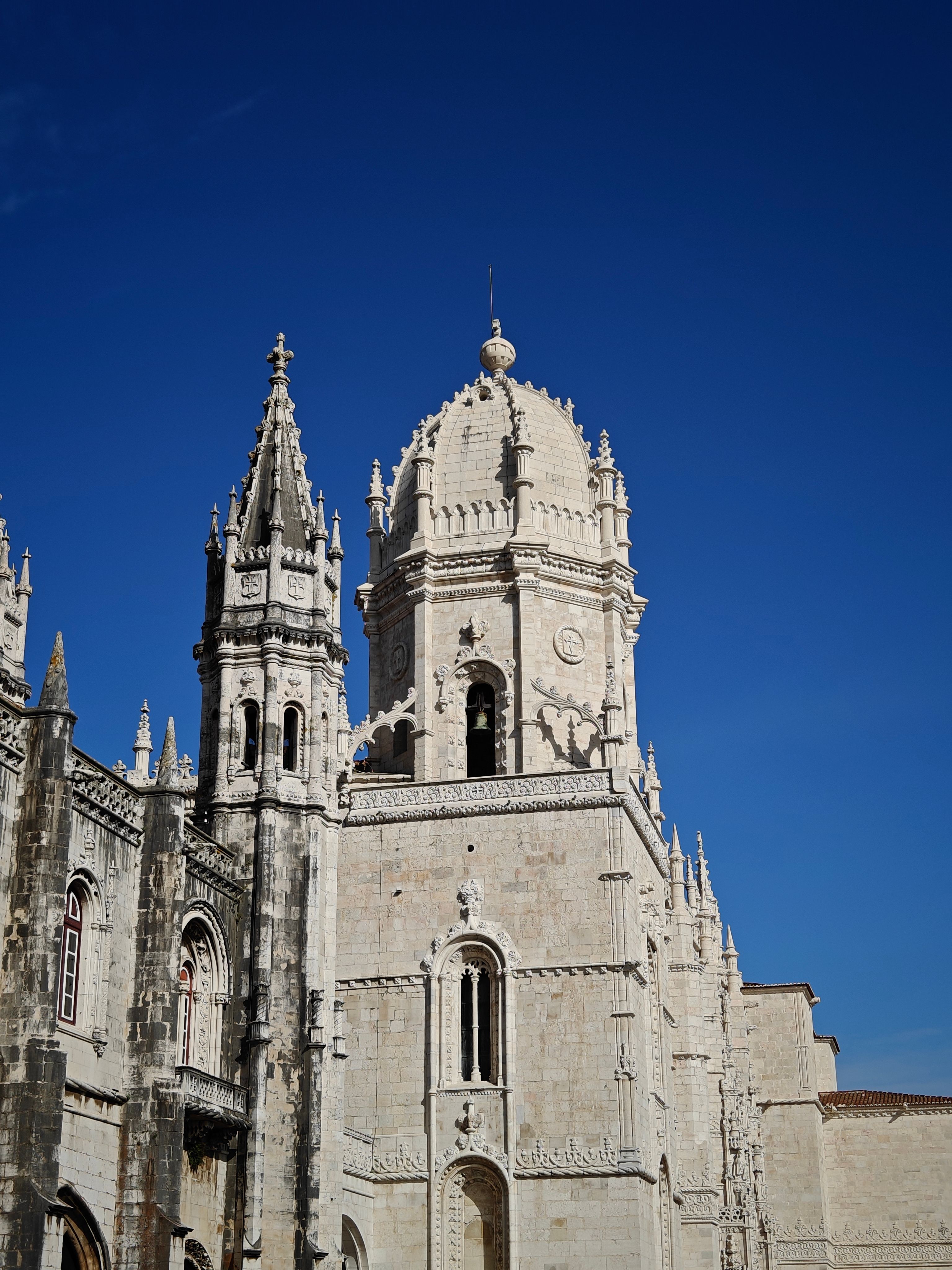A majestic Gothic tower from Jerónimos Monastery under a vivid blue sky in Lisbon, Portugal.